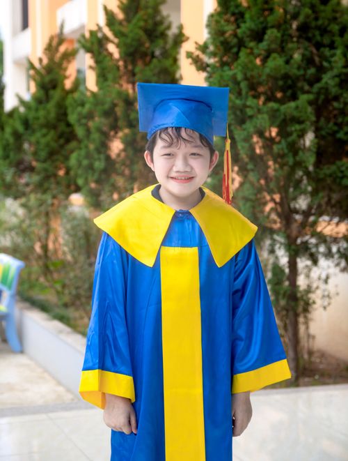 Free A young boy wearing a blue and yellow graduation gown smiles outdoors. Stock Photo