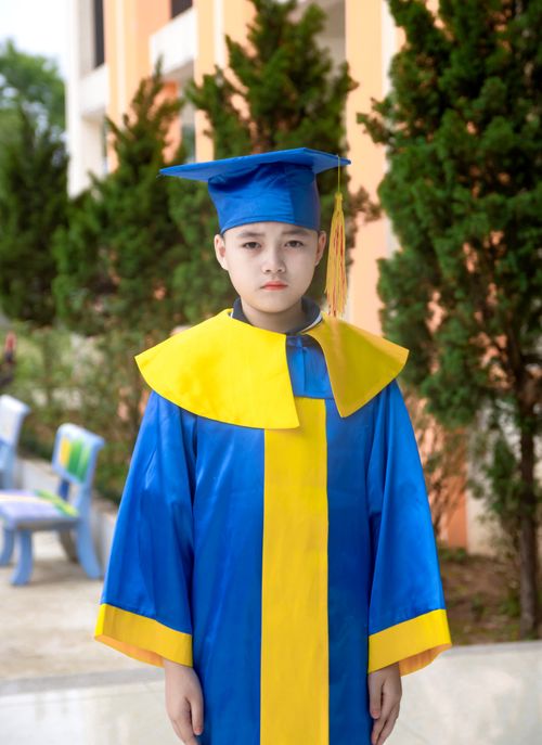 Free A child wearing a blue and yellow graduation gown standing outdoors near greenery. Stock Photo