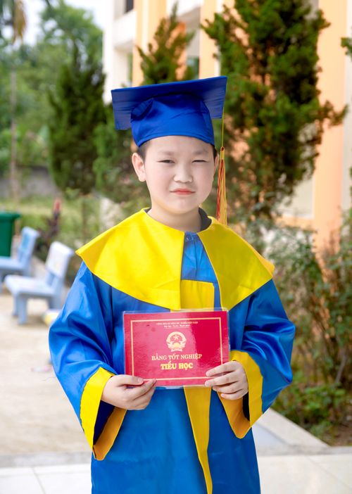Free A young Asian child in graduation attire holding a diploma outside. Stock Photo