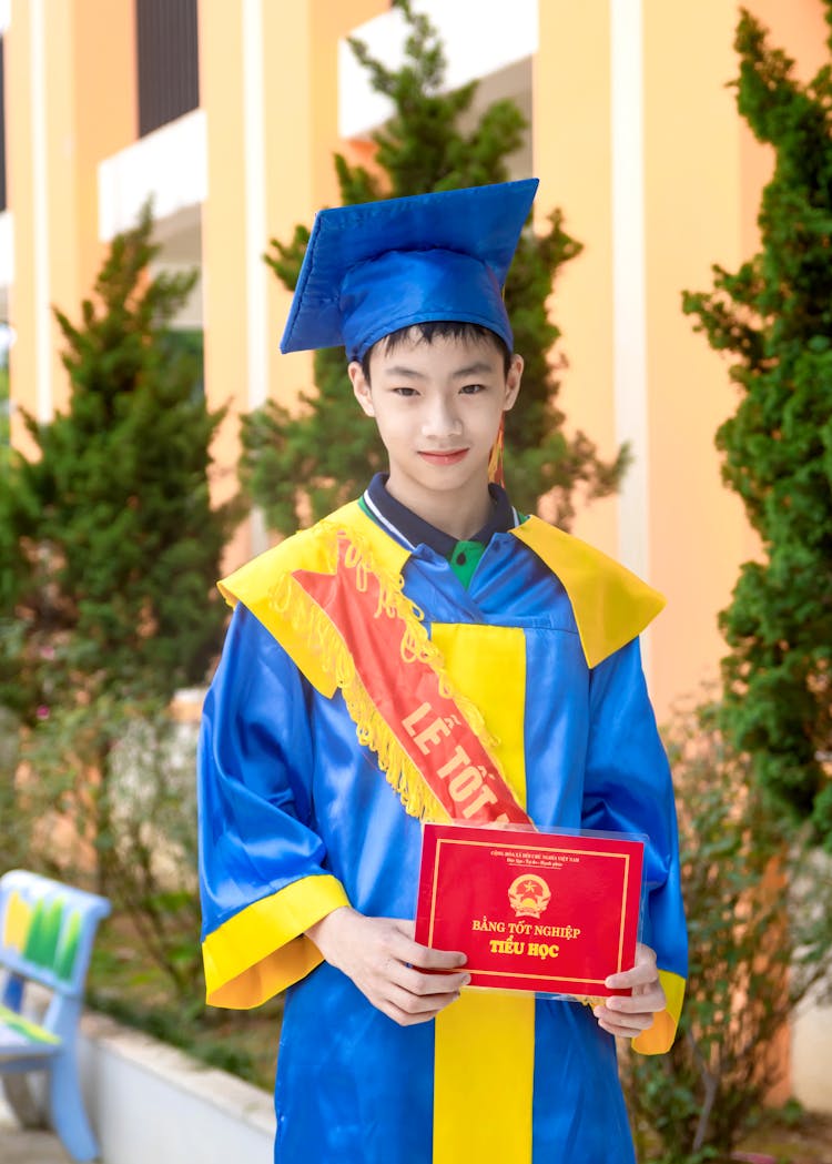 Boy Wearing A Graduation Gown And Sash Holding A Certificate