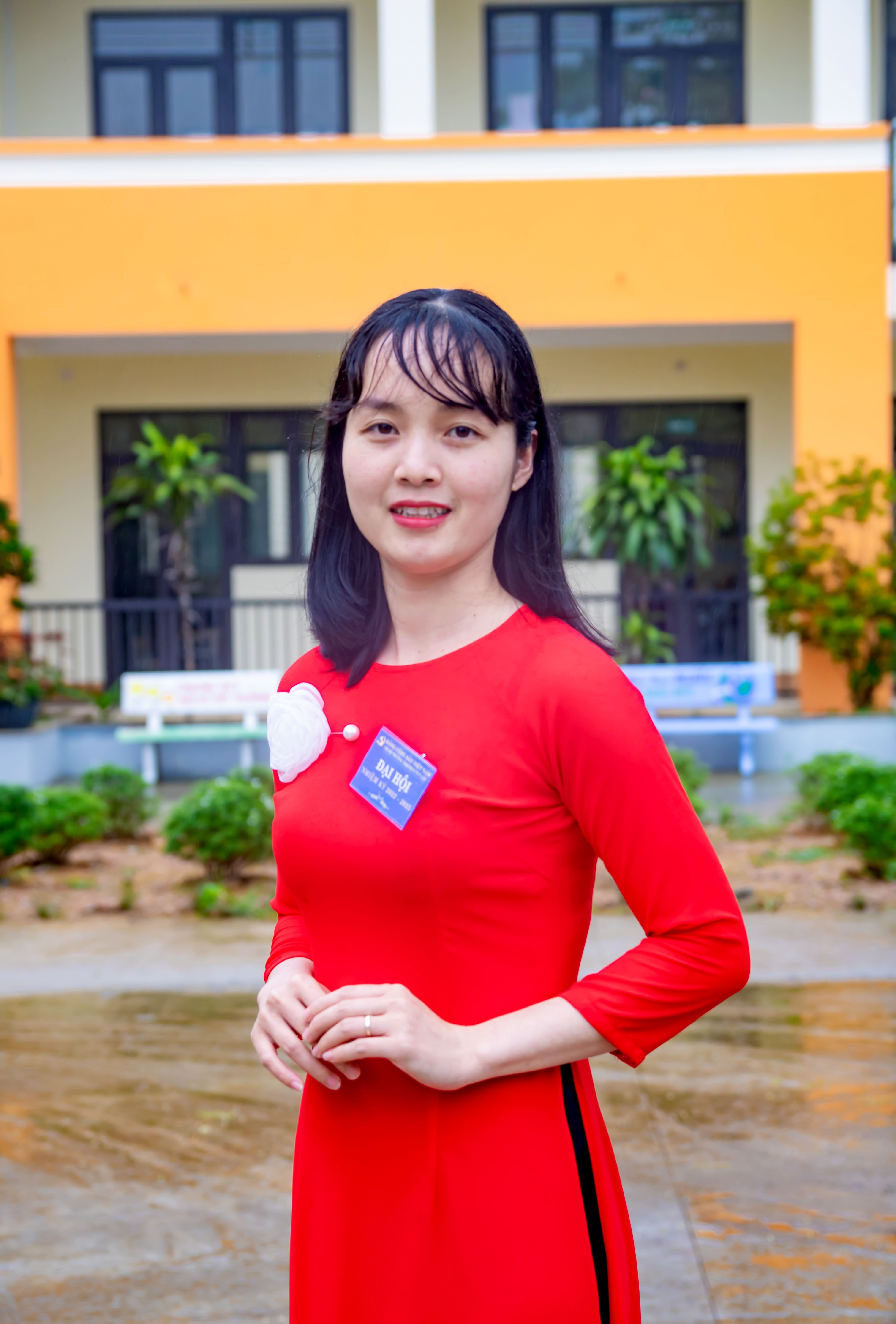 Smiling woman in a red dress posing outdoors in front of a building.