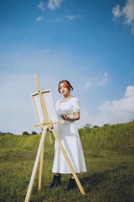 Portrait of a woman painting in a meadow with an easel on a sunny day.