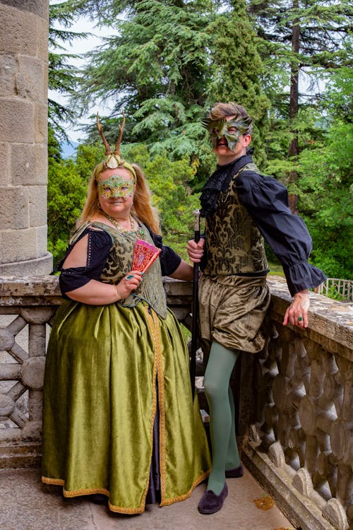 Young Man and Woman Wearing a Mask and Medieval Costumes Posing on Concrete Balcony