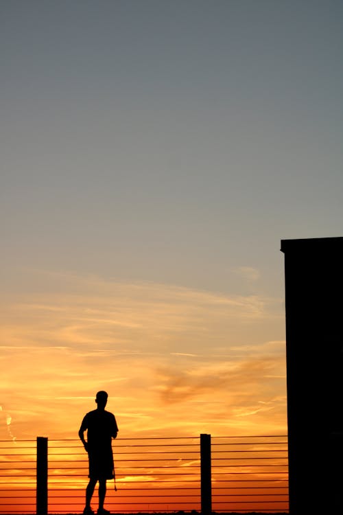 Silhouette of Person Standing on Balcony during Sunset