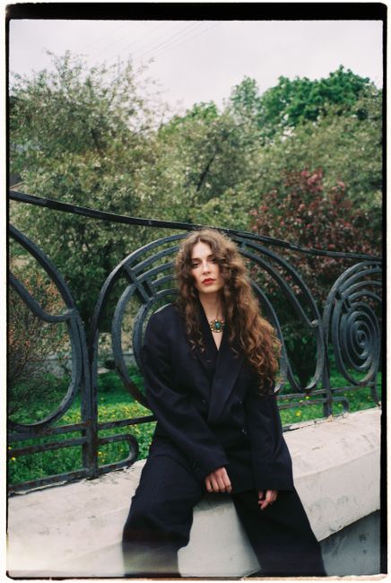 Fashionable woman poses elegantly in a lush outdoor setting wearing a chic suit.