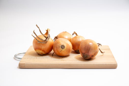 Five fresh onions neatly arranged on a wooden cutting board against a white background.