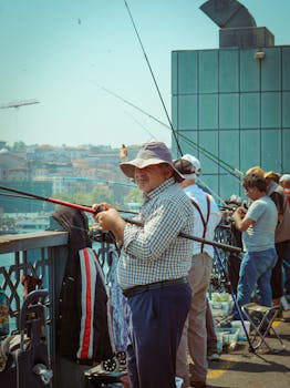 Group of people fishing on a city bridge, using fishing rods under clear sky.