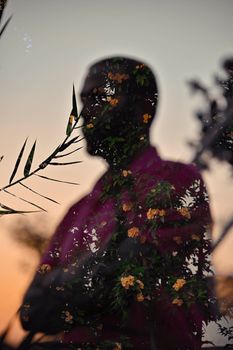 Artistic double exposure silhouette blending flowers and a man's profile at sunset.