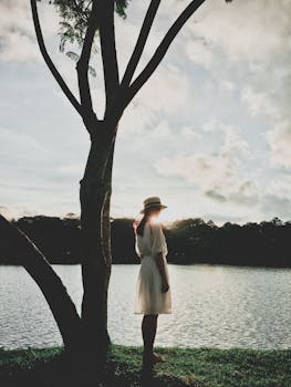 日落时分，一位戴帽子的女子站在湖边，营造出宁静的氛围