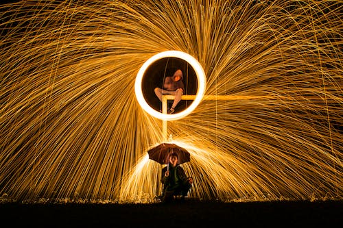 Time Lapse Photography of Person Making Firework Spark Under Person Holding Umbrella during Nighttime