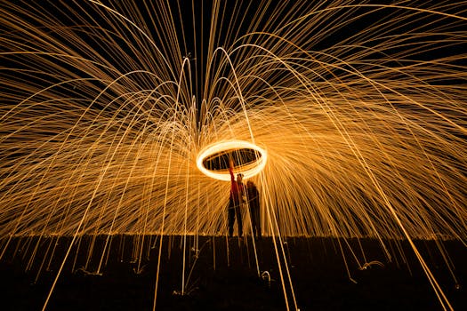 Dramatic long exposure of steel wool light painting with glowing trails and silhouetted figures.