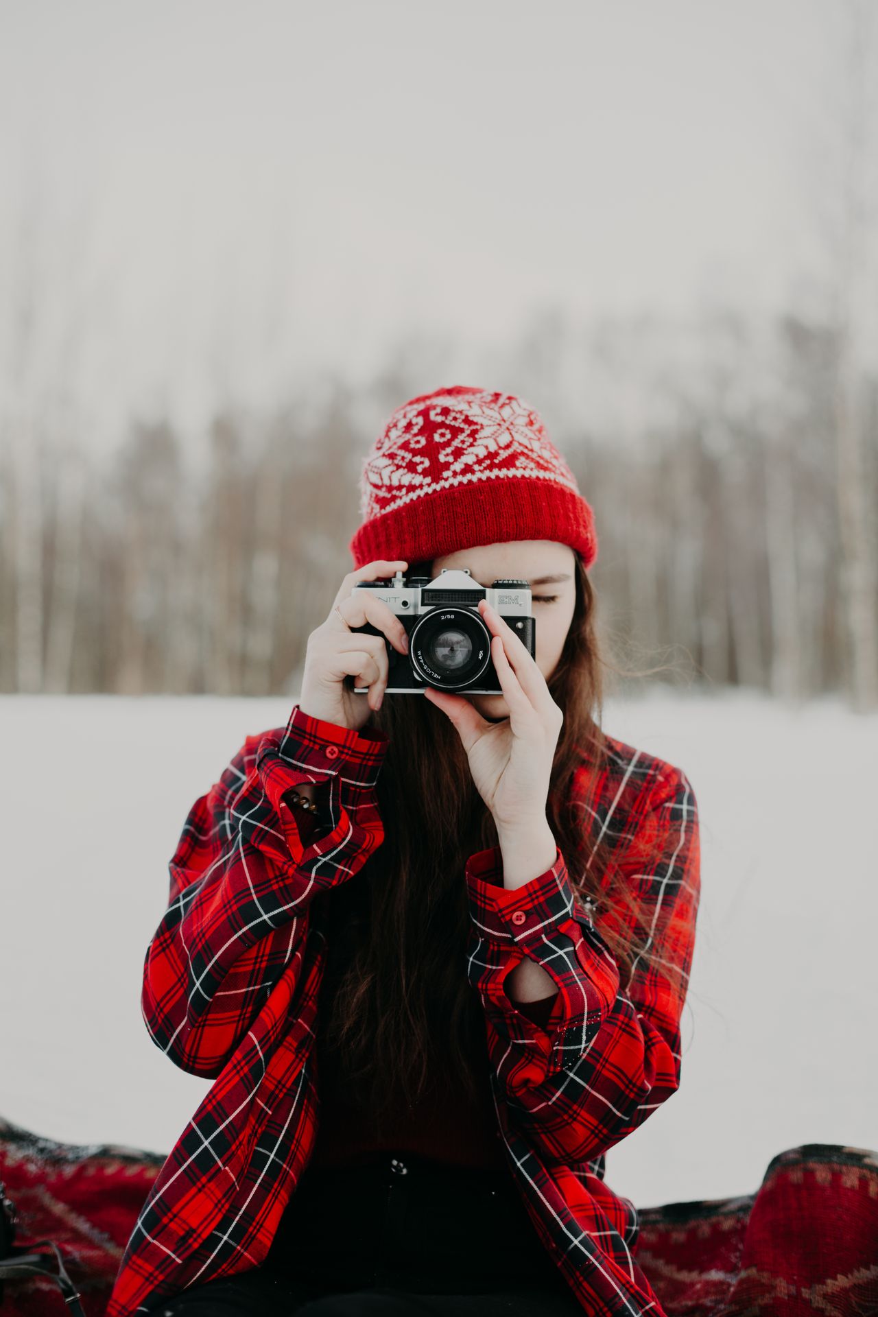 Woman in a red fair-isle beanie holding a camera in the snow