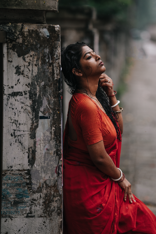 Free Contemplative woman in vibrant red sari gracefully leans against a weathered wall. Stock Photo