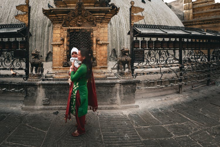 Woman In Traditional Clothes With Baby Near Old Temple