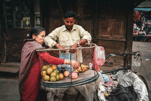 Free A man and woman interact at a fruit market in Kathmandu, Nepal, showcasing local street life. Stock Photo