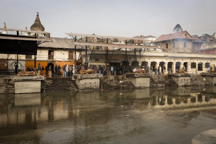 People Lining Up On Street By River Shore