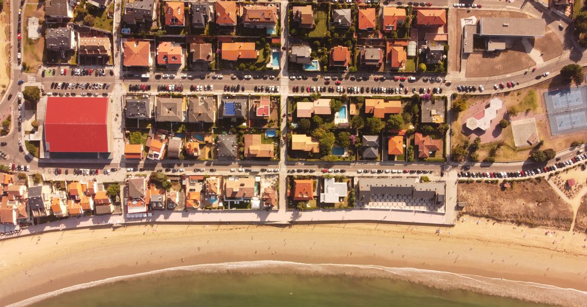Drone shot capturing a picturesque seaside neighborhood in Nigrán, Spain with vibrant houses and sandy beach.