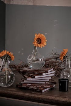 Aesthetic arrangement of sunflowers in vases atop stacked books on a rustic desk.