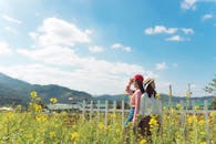 两名妇女站在栅栏旁，在黄色的花田里享受着阳光明媚的乡村时光