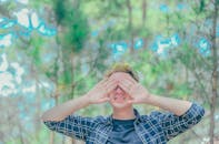 阳光明媚的公园里，一个年轻人开玩笑地用手捂住了脸