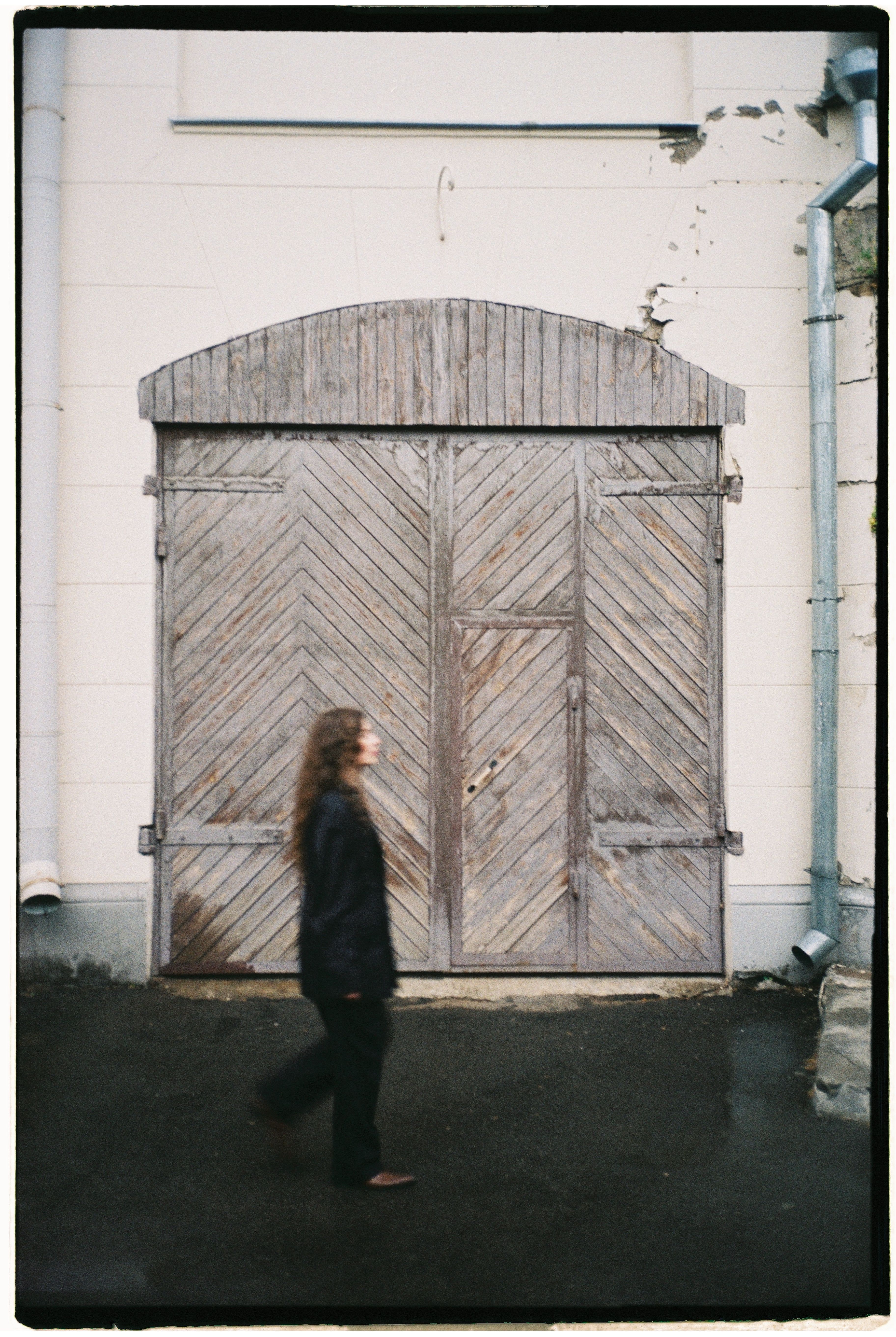 A woman walks past a large, rustic wooden barn door, adding motion and elegance to a classic setting.