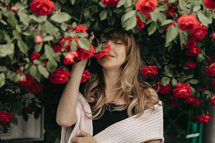 Blonde Woman Smelling Flowers Under Rose Bush