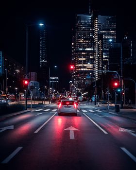 Warsaw city street at night with car and illuminated skyscrapers. Vibrant urban life captured after dark.