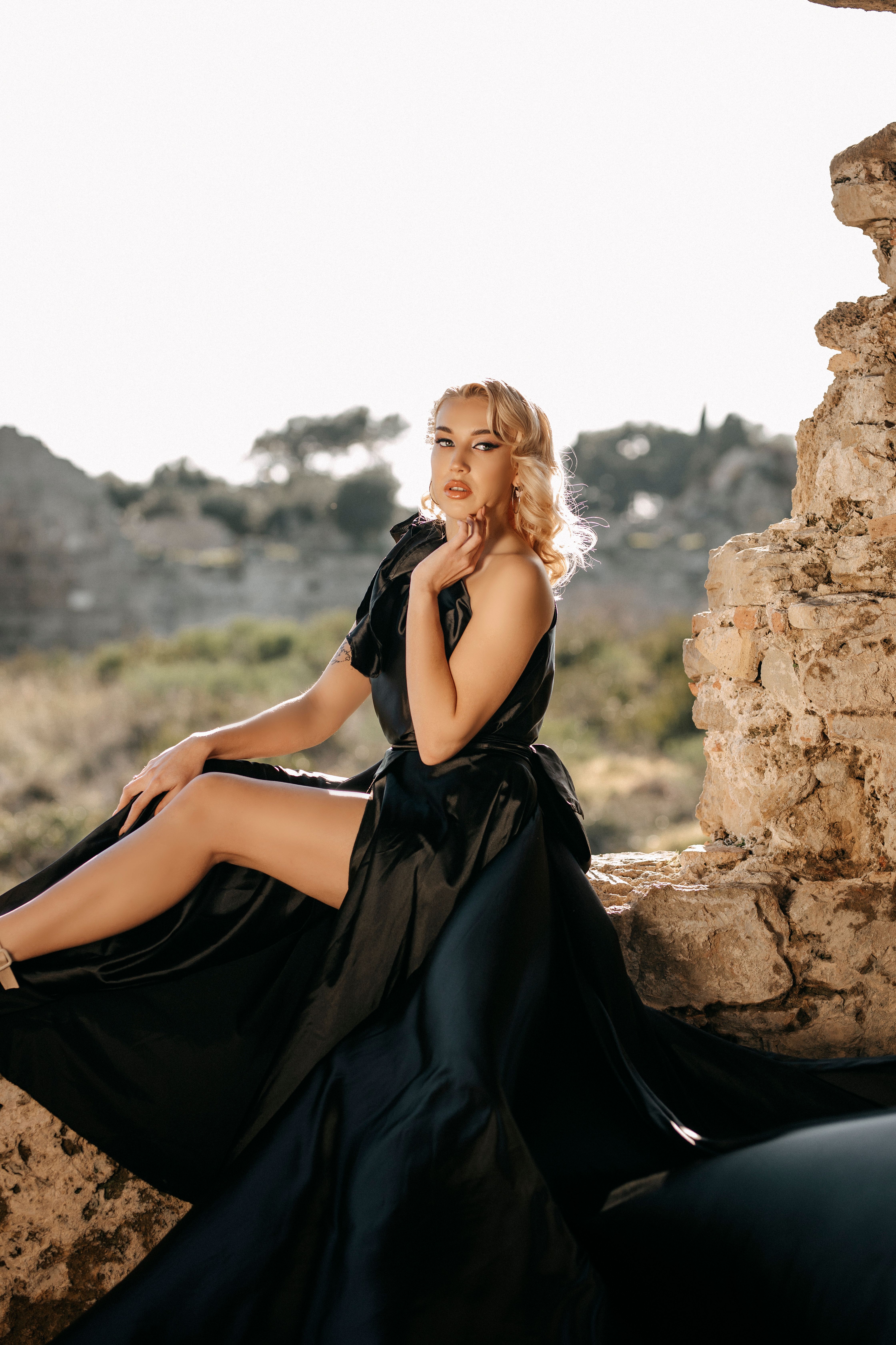 A fashionable woman in a flowing black dress poses gracefully among ancient ruins.