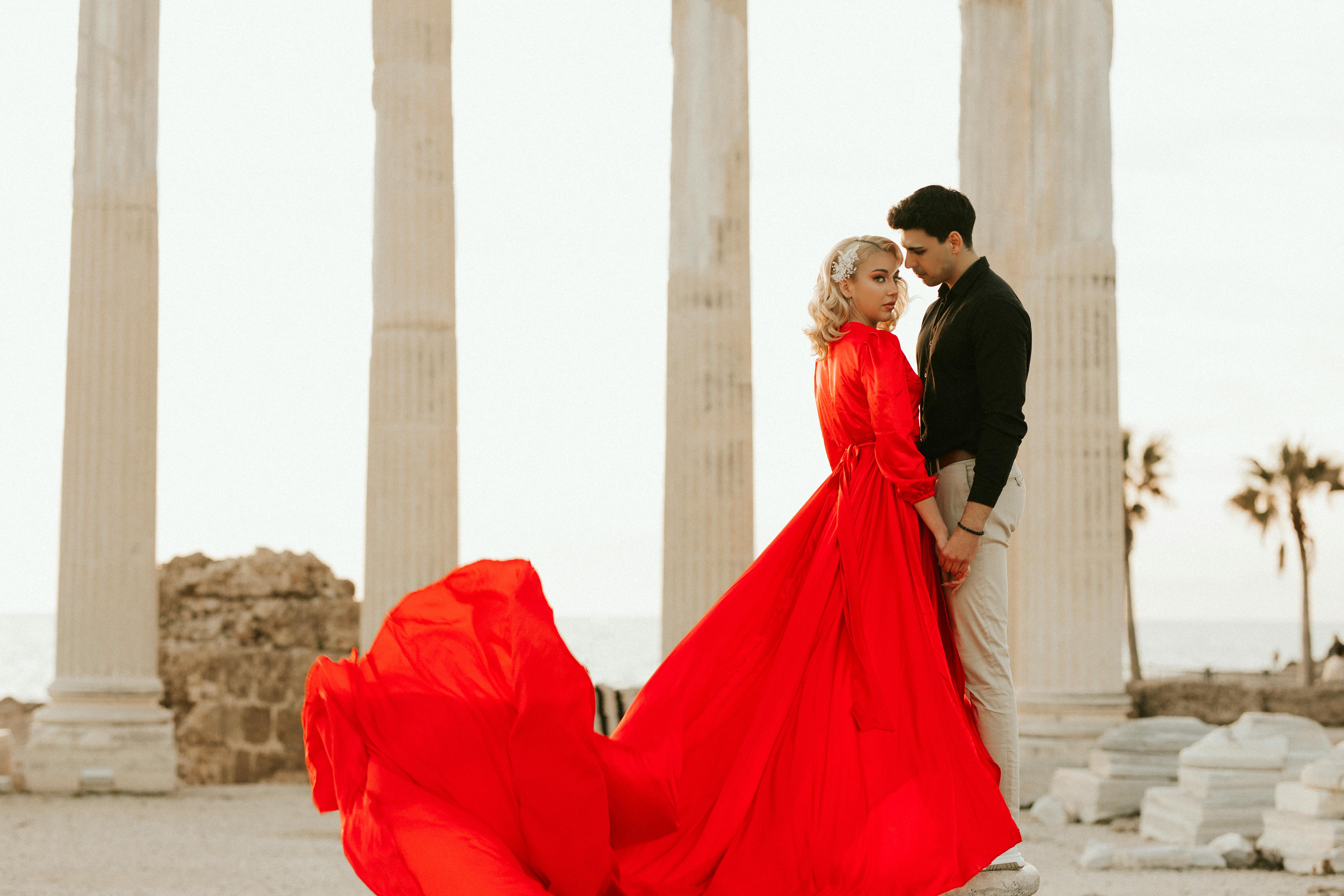 woman in red long dress standing with a man in black long sleeve shirt