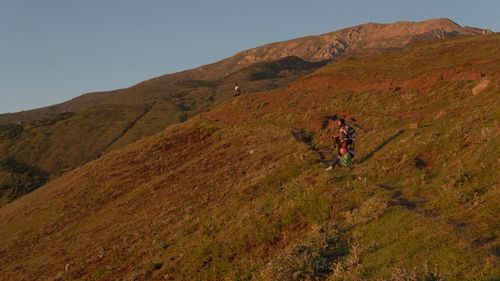 Free A serene scene of hikers enjoying a sunset view on a hillside trail with majestic mountain backdrop. Stock Photo