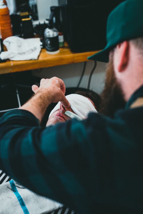Free Close-up of a barber expertly shaving a man's face in a modern barbershop. Stock Photo