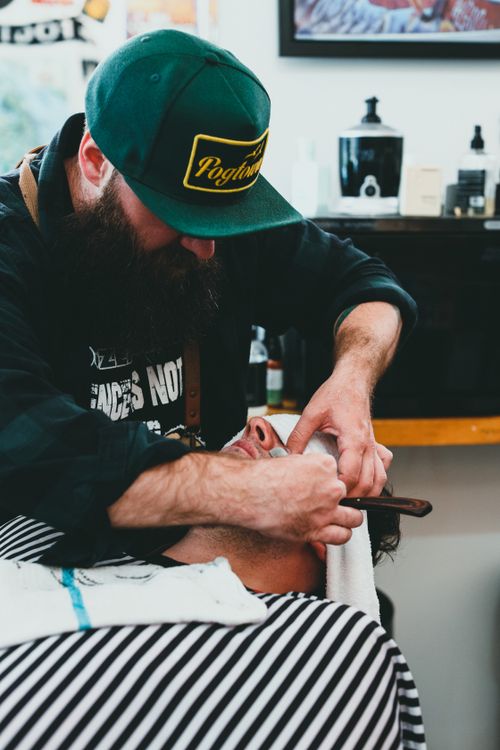 Free Barber shaving a client's beard with a straight razor in a classic barber shop setting. Stock Photo