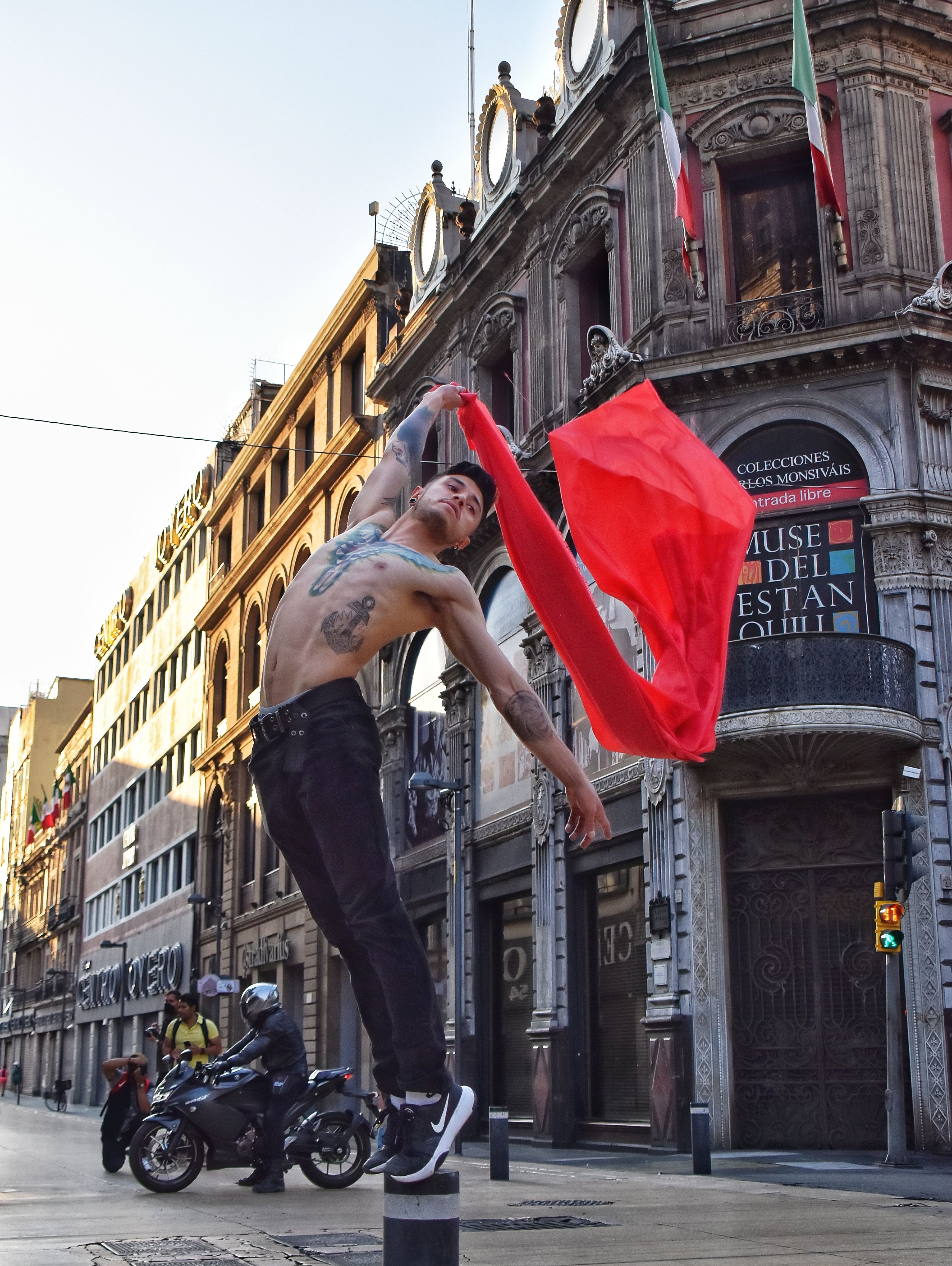 A man performs a dynamic pose with a red cloth in the urban streets of Mexico City.