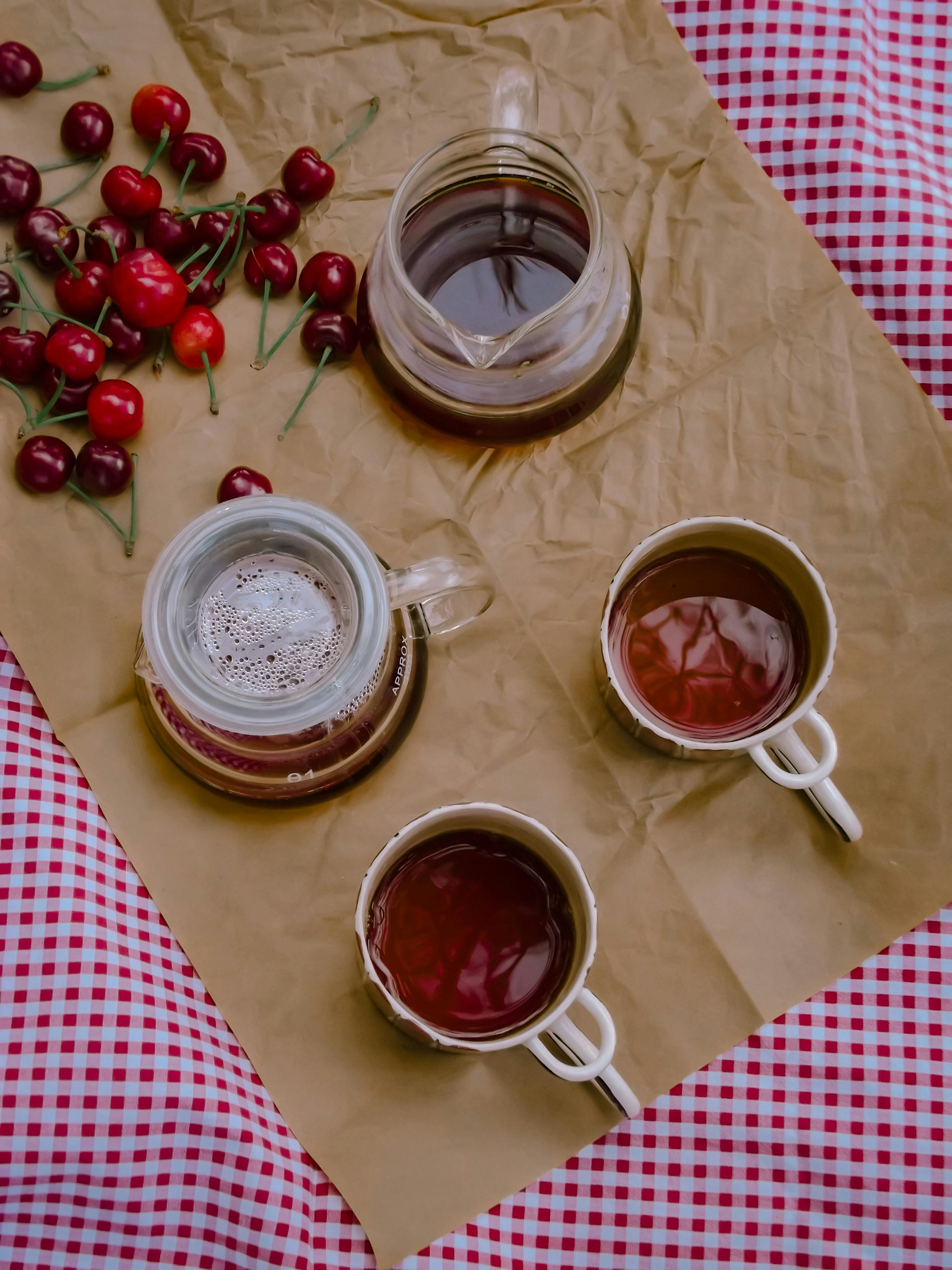 Still life of cherries and tea cups on a gingham tablecloth, cozy setup.