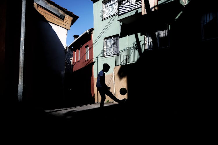 A Silhouette Of A Boy Kicking A Ball