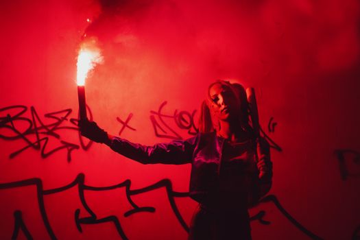 A striking image of a person holding a flare against a graffiti-covered wall, illuminated by red light.