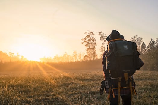 A lone backpacker gazes at a sunrise over a foggy field, embracing adventure.
