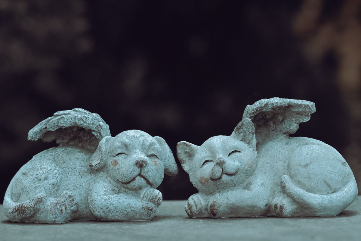 Deux statuettes de jardin en pierre, un chien et un chat endormis avec des ailes d'ange