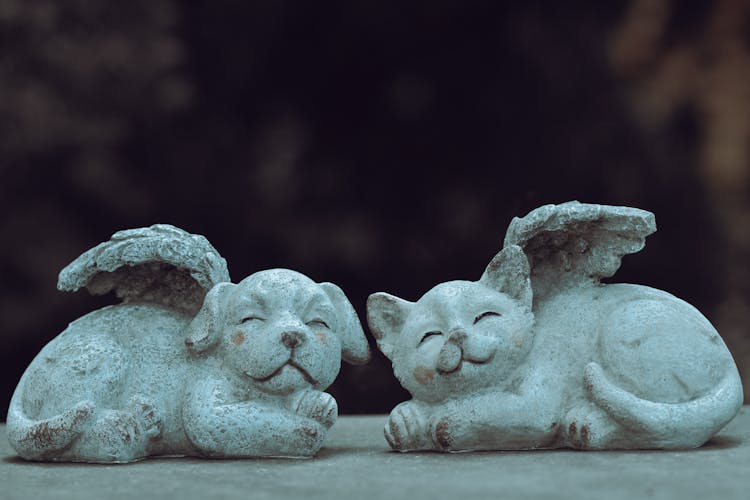 A Gray Ceramic Figurine Of A Dog And Cat With Tiny Wings