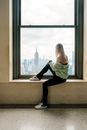 Girl in Green Long Sleeve Shirt and Black Pants Sitting on Window