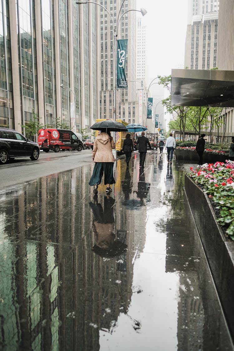 A Person Holding An Umbrella Walking Near Tall Buildings
