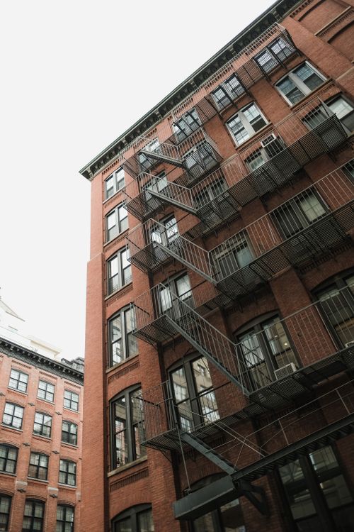 Free A red brick building with a fire escape in an urban area, showcasing classic architecture. Stock Photo