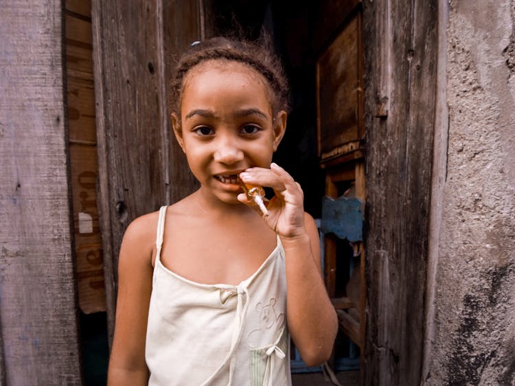 Cute Girl Near Poor Stone House Eating Lollipop