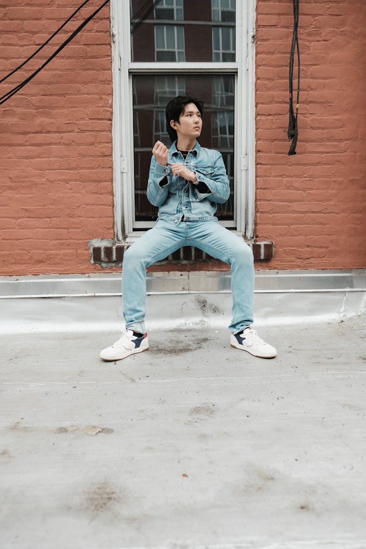 A Man In Denim Wear Sitting On A Window Sill