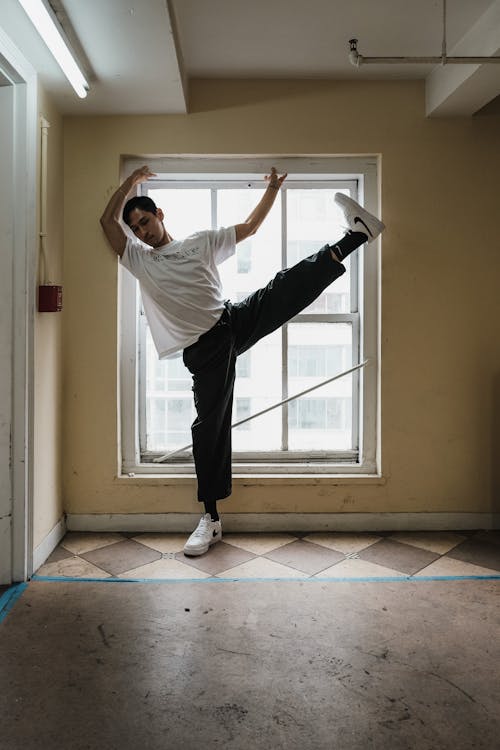 Man in White Shirt and Black Pants Standing in Front of Window