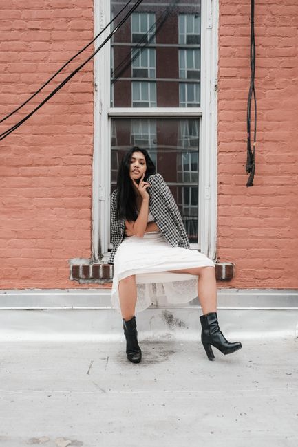 Fashion model in tulle skirt and boots sitting on rooftop in city setting.