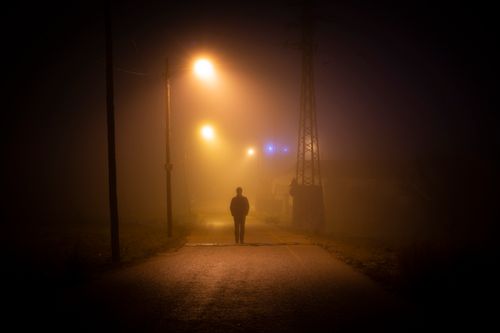 Free Silhouette of a lone person walking on a misty, dimly lit street in Madrid at night. Stock Photo
