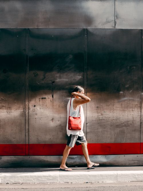 Free A man in casual attire walks along an urban street, carrying a red bag. Stock Photo
