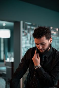 A man in formal attire engages in a phone call indoors, exuding professionalism.