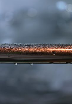 Detailed view of a metallic pipe covered with raindrops against a blurred background.